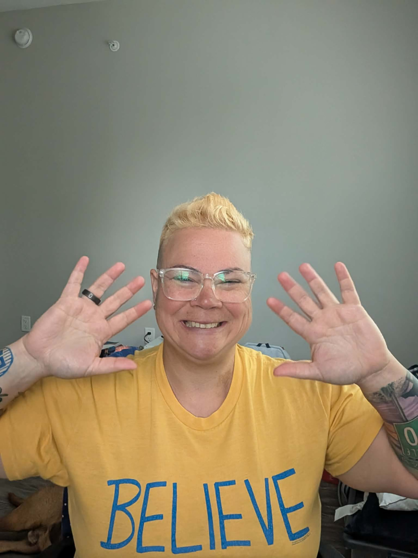 Juli laughing with both hands up in a BELIEVE t-shirt